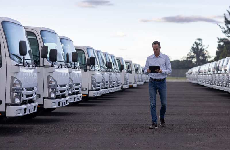Man walking through a fleet of parked trucks, using a tablet to manage or assess vehicles