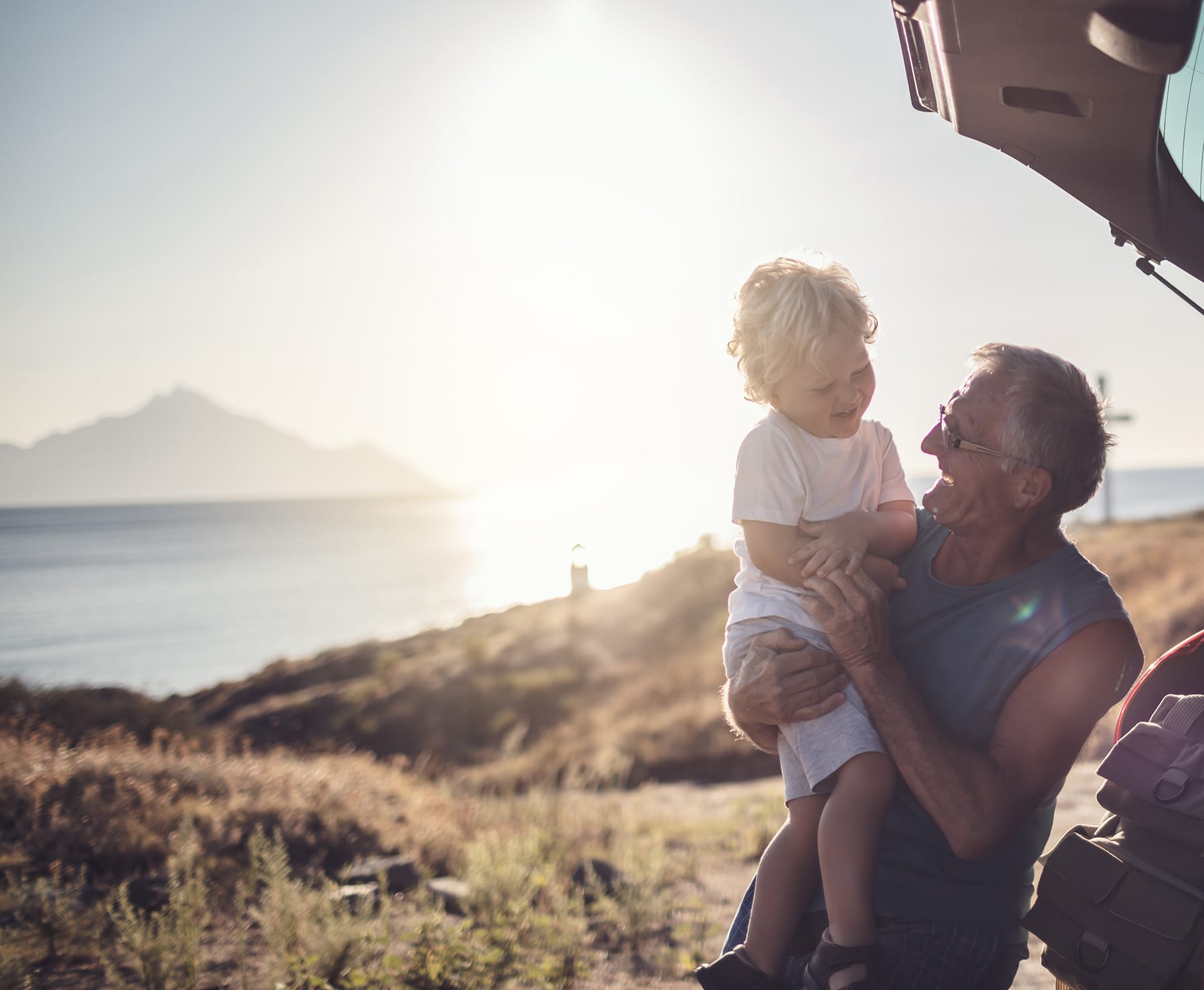 A joyful moment between a grandparent and child by the beach during sunset, highlighting family connection and warmth