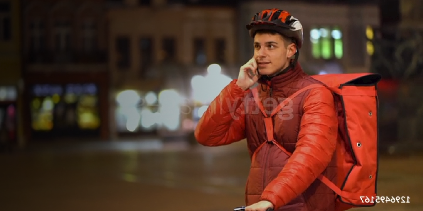 Delivery cyclist on the phone, preparing for a nighttime food delivery in an urban setting