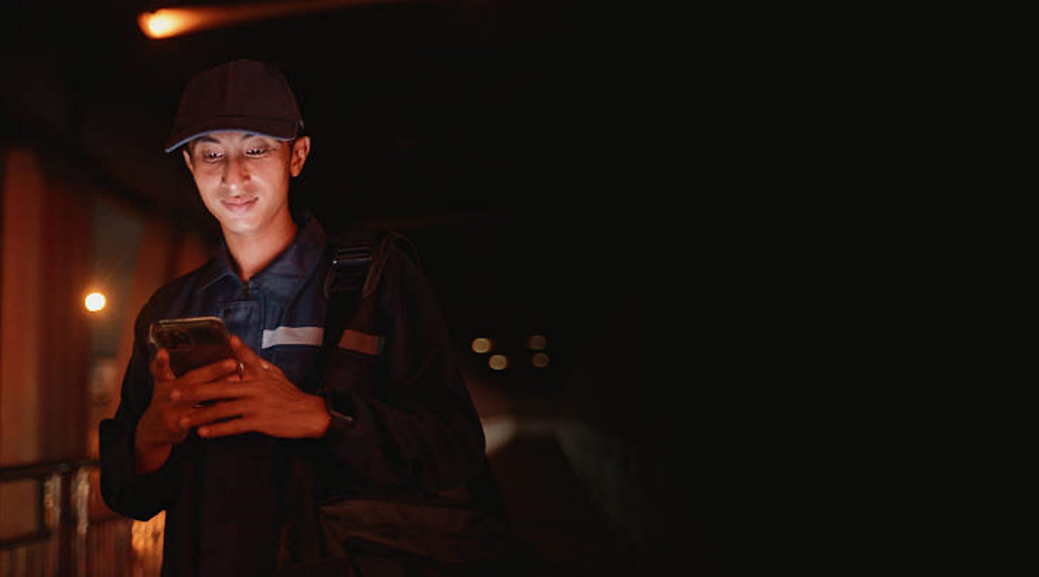 A person checks their phone while standing in a dimly lit area, suggesting communication or waiting for instructions