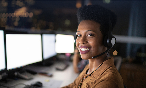 A customer support agent smiling while working at a computer station with multiple screens in a modern office