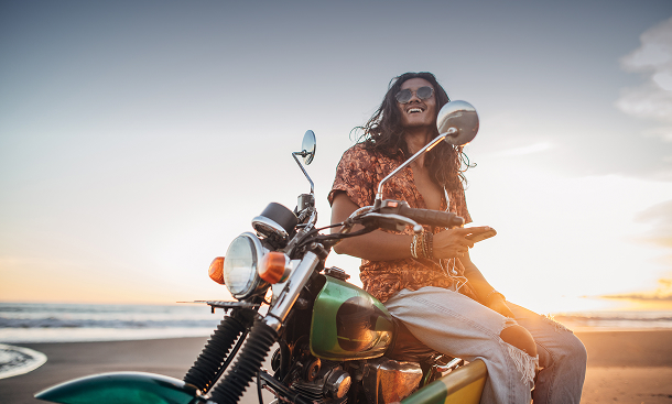 A person enjoying a sunset while sitting on a motorcycle at the beach, holding a smartphone