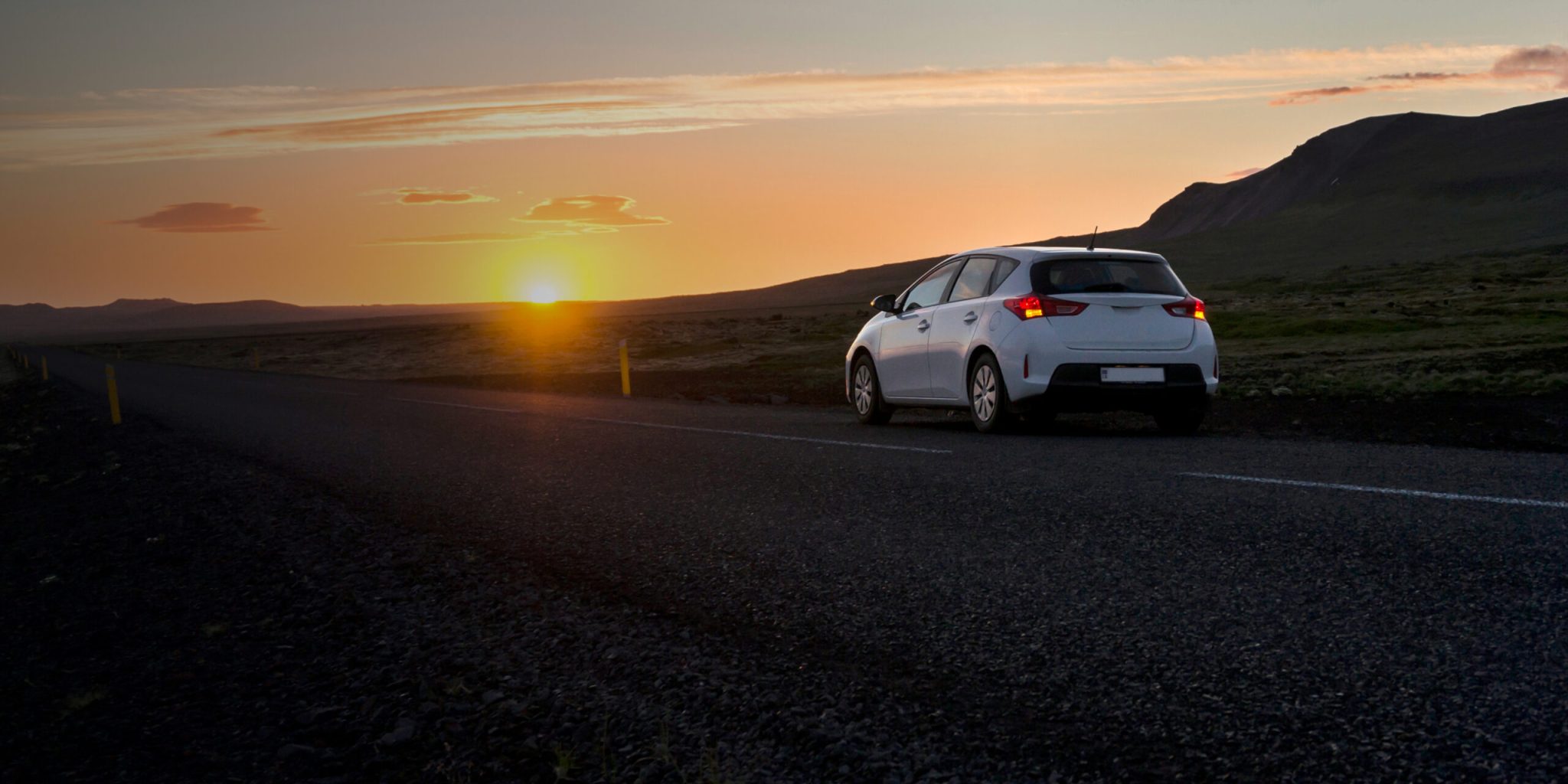 A car parked on a road at sunset, representing a travel destination or adventure