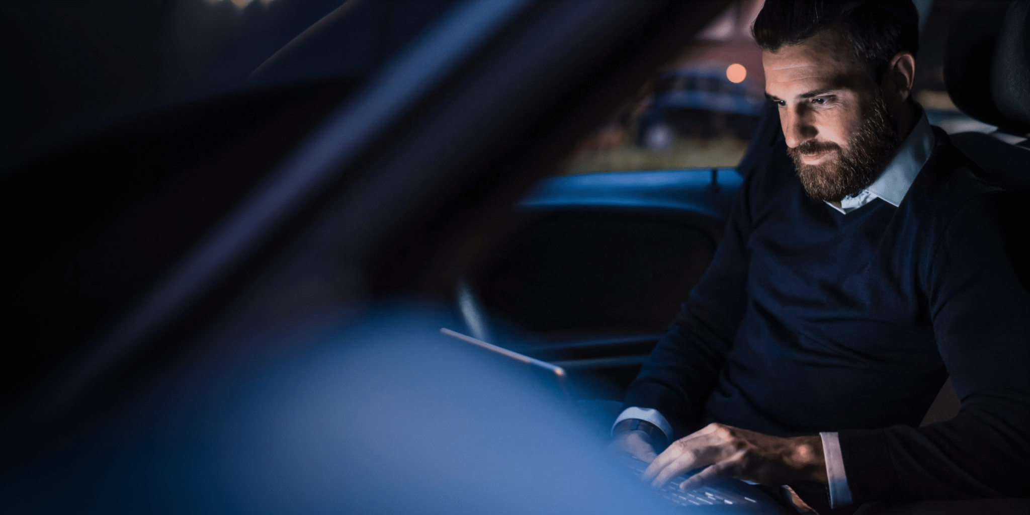 Man working on a laptop inside a car at night, focused on his task