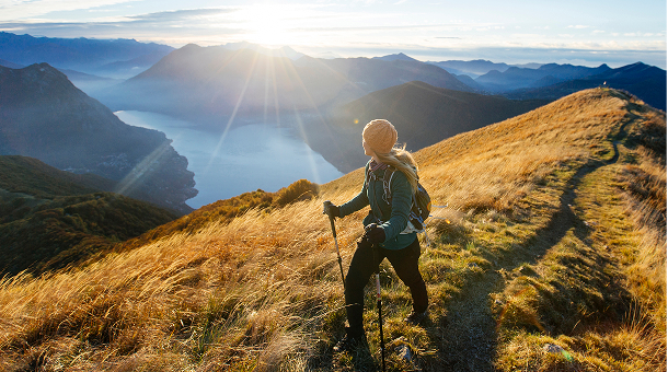 Hiker on a mountain trail overlooking a lake and distant mountains during sunrise