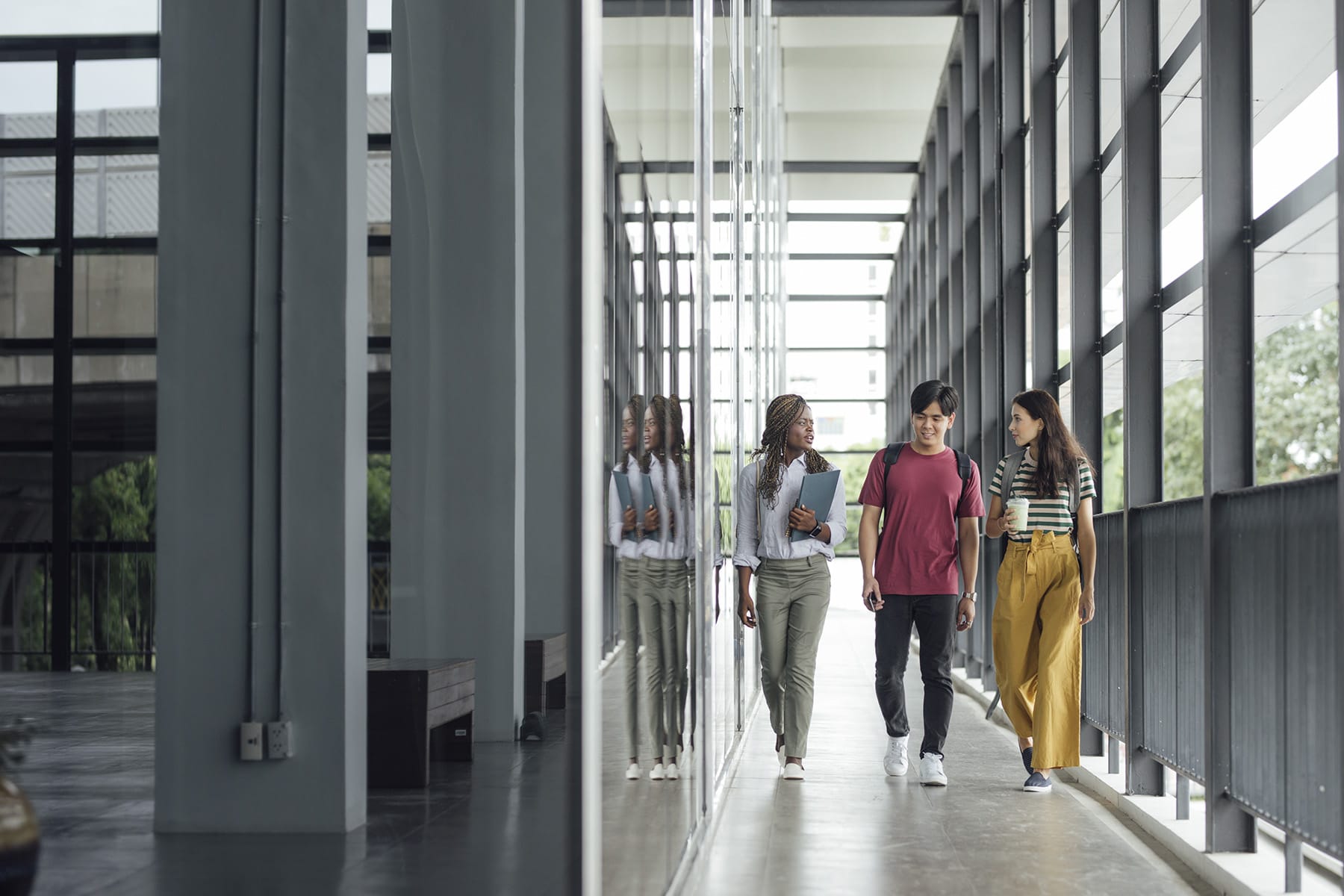 Three students walking and chatting in a modern building corridor, reflecting a collaborative atmosphere